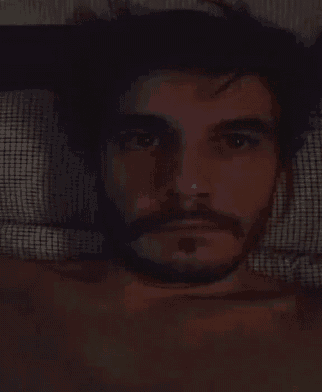 a man with a beard is sleeping in a bed with his eyes closed .
