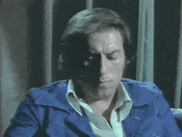a man in a blue jacket is sitting in front of a curtain