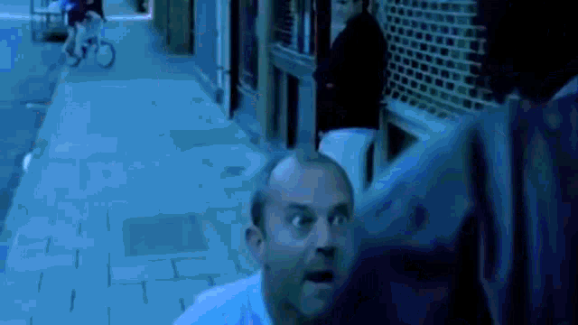 a man in a white shirt is standing on a sidewalk with his mouth open and looking at something .
