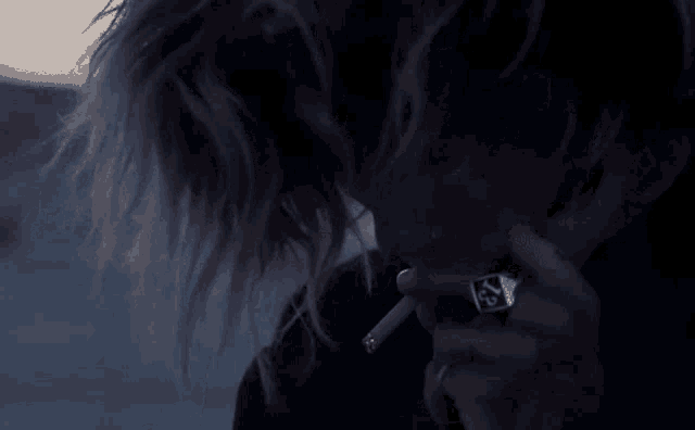 a woman is smoking a cigarette in the dark with a ring on her finger .
