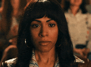 a woman wearing hoop earrings looks at the camera with a serious look on her face