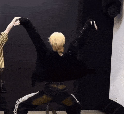a man with blonde hair is kneeling down with his arms outstretched in a dance pose .