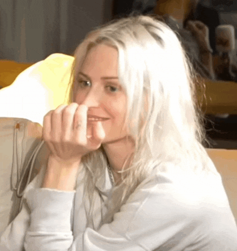 a woman with blonde hair is sitting on a couch with her hands on her chin