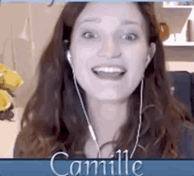 a woman wearing ear buds is smiling in front of a sign that says camille