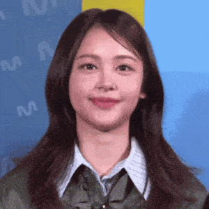 a woman wearing a green jacket and a blue shirt smiles