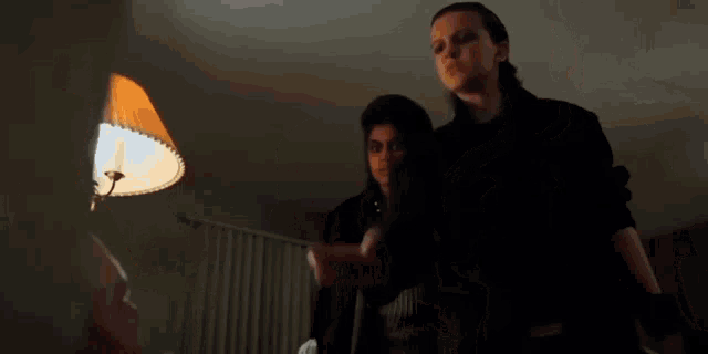 a couple of people standing next to each other in a dark room with a lamp .