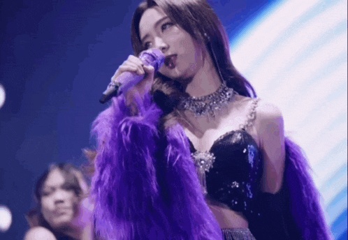 a woman is singing into a microphone while wearing a purple fur coat .