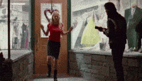 a woman in a red shirt is dancing in front of a man with a gun .