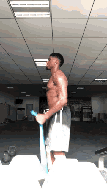 a shirtless man is standing in a gym holding a blue rubber band