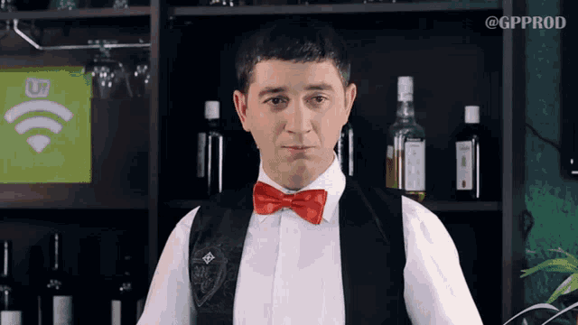 a man wearing a red bow tie is standing in front of a shelf with bottles of alcohol on it