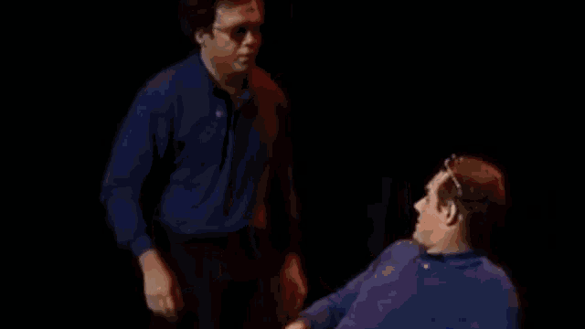 a man in a blue shirt is shaking hands with another man in a blue shirt