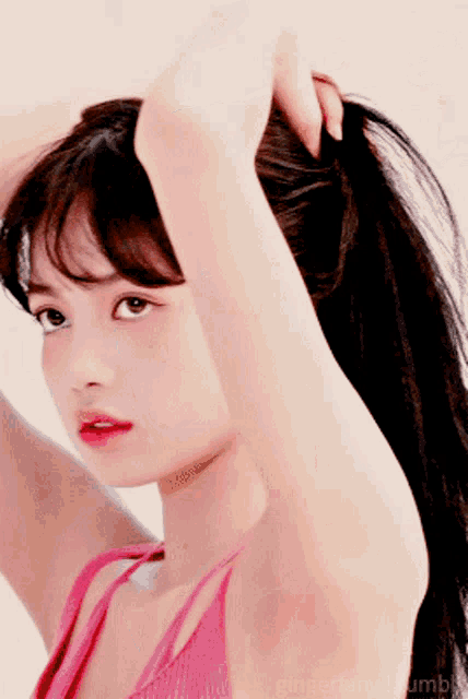 a woman in a pink tank top is holding her hair up