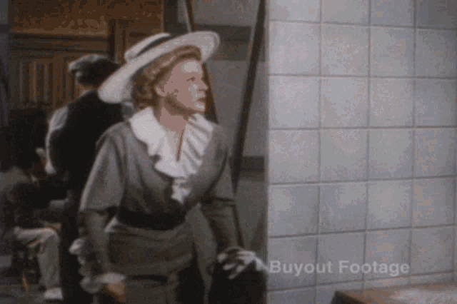 a woman in a hat is standing in front of a tiled wall with buyout footage written on it