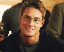 a man wearing glasses and a gray shirt is smiling for the camera .