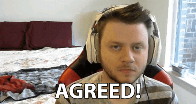 a man wearing headphones says agreed while sitting in front of a bed