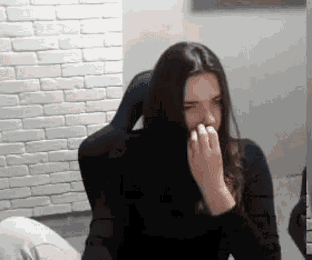 a woman with long dark hair is sitting in a chair covering her mouth with her hand .
