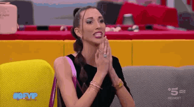 a woman is sitting on a couch with her hands folded in prayer