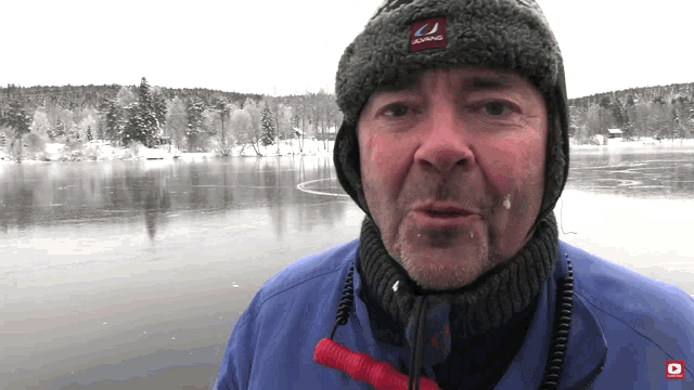 a man wearing a hat that says ulvang on it stands in front of a frozen lake