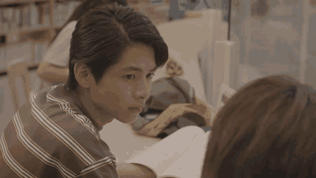 a man in a striped shirt sits at a desk with a book
