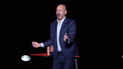 a bald man in a suit is standing on a stage with his arms outstretched .
