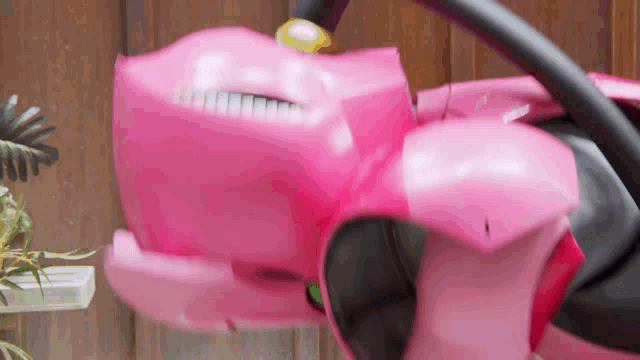 a close up of a pink toy car with a steering wheel on a wooden fence