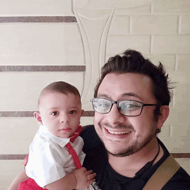a man wearing glasses is holding a baby and smiling