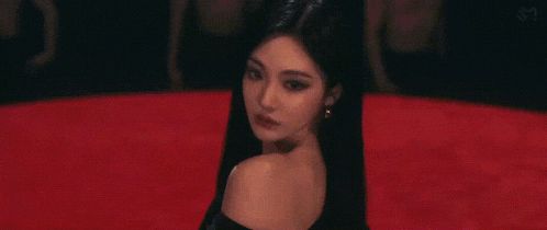a woman in a black dress is standing on a red carpet in a dark room .