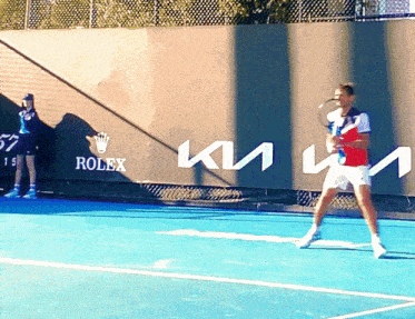 a man is playing tennis on a court with a rolex sign behind him
