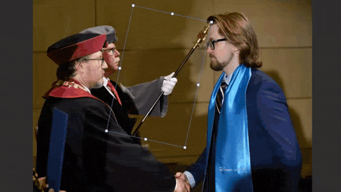 a man in a blue scarf shakes hands with a man in a graduation gown