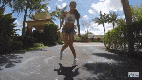 a woman in shorts and a crop top dancing on a street with a like button in the corner