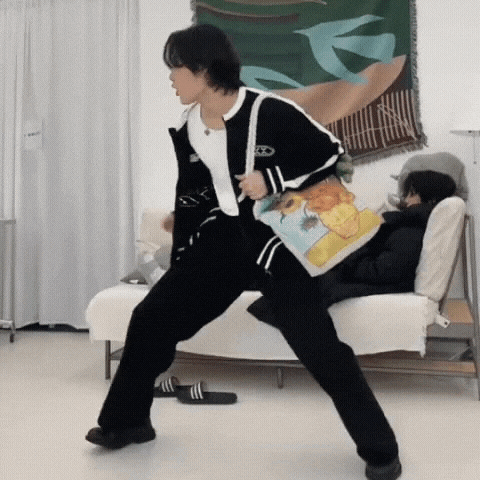 a man in a black jacket and black pants is dancing in a living room while holding a bag .