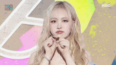 a woman with blonde hair is eating a lollipop in front of a sign that says mbc on it