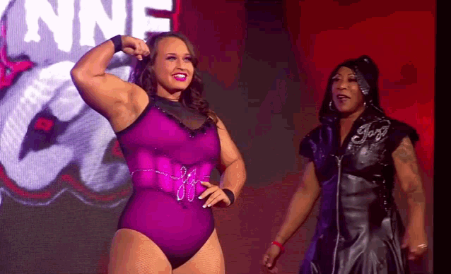 a woman in a purple leotard flexes her muscles next to another woman in a black dress .