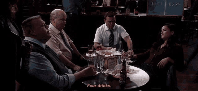 a group of people are sitting around a table with a sign that says four drinks on it