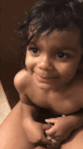 a baby without a shirt is smiling while sitting on a person 's lap