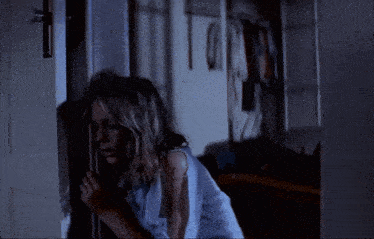 a woman in a blue shirt is standing in a doorway in a dark room