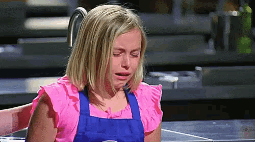 a little girl in an apron is crying in a kitchen .