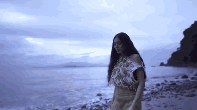 a woman with long hair is standing on a beach near the water