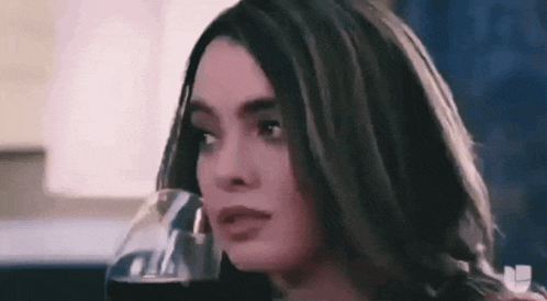 a woman is holding a glass of wine in her hand and looking at the camera .