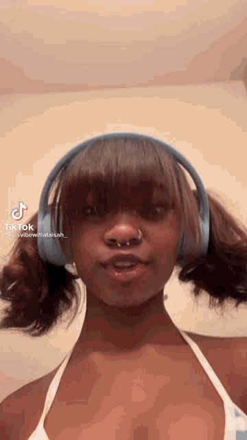a woman wearing headphones and a nose ring is looking at the camera .
