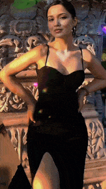 a woman in a black dress standing in front of a stone wall
