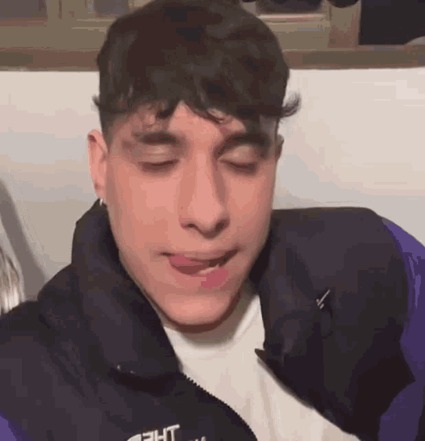 a young man wearing a purple jacket and a white t-shirt is making a funny face .