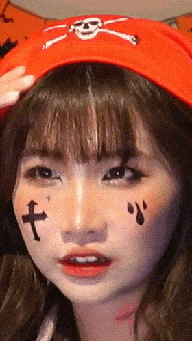 a close up of a girl wearing a red hat with a cross on her face