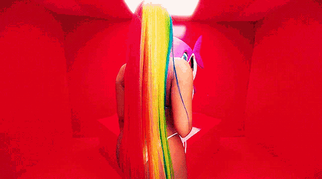 a woman with rainbow hair is standing in a red room with a fish in the background .