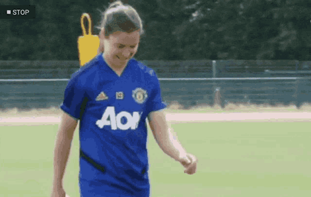 a girl wearing a blue aoi jersey stands on a soccer field