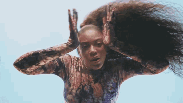 a woman with long curly hair is wearing a floral shirt and gloves