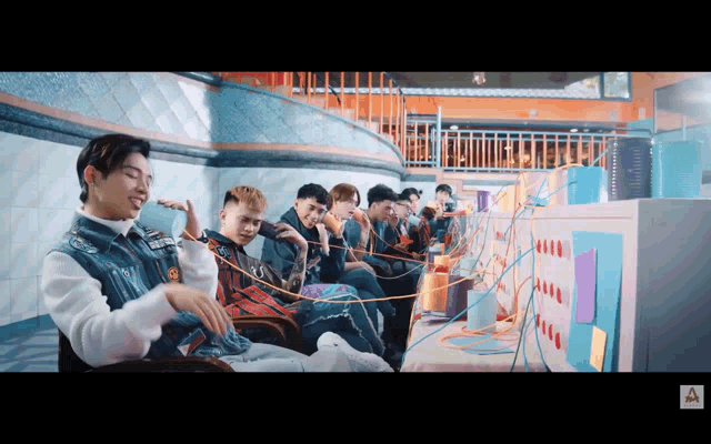 a group of young men are sitting in front of a computer screen with the letter a on the bottom left