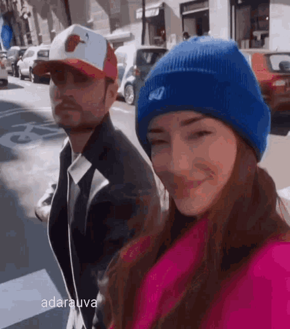 a man and a woman are walking down the street and the woman is wearing a blue beanie .