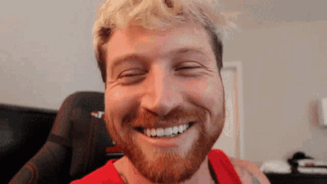 a man with a beard wearing a red tank top is smiling with his eyes closed