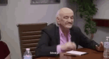 an older man in a suit is sitting at a table with a bottle of water .